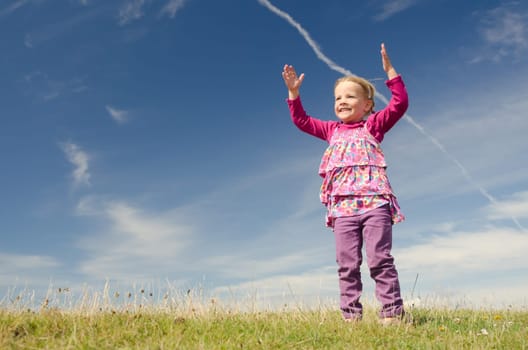 Young girl jumping on a green meadow against blue sky