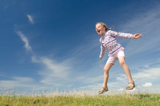 Young girl jumping on a green meadow against blue sky