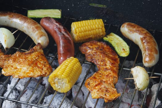 colorful grilled food on a charcoal grill with meat,sausages,corn,zucchini and onion