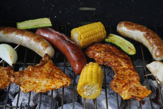 colorful grilled food on a charcoal grill with meat,sausages,corn,zucchini and onion