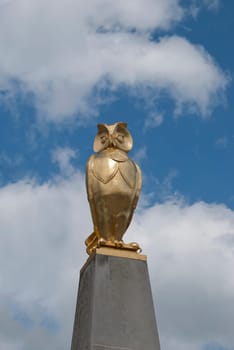 A Gold Coloured Statue of an Owl against a summer sky