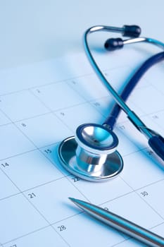 Routine medical exam represented by part of stethoscope, calendar and pen. Family doctor workplace.