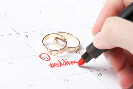 Wedding rings and hand writing word wedding into calendar