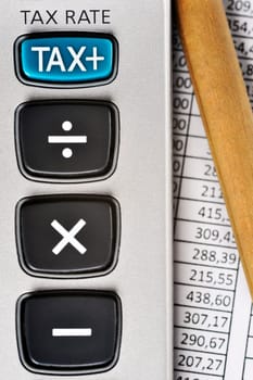 Detail of calculator, focusing the TAX key, next to a sheet of paper with numbers and a pencil.