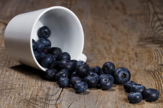Blueberries rolling from overturned cup on wooden background