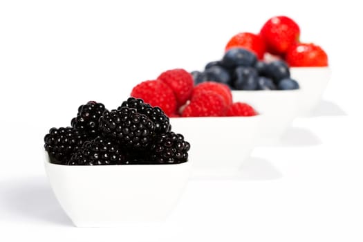 Blackberries in a bowl in front of other berries on white background