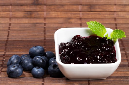 Blueberries jam next to blueberries on wooden background