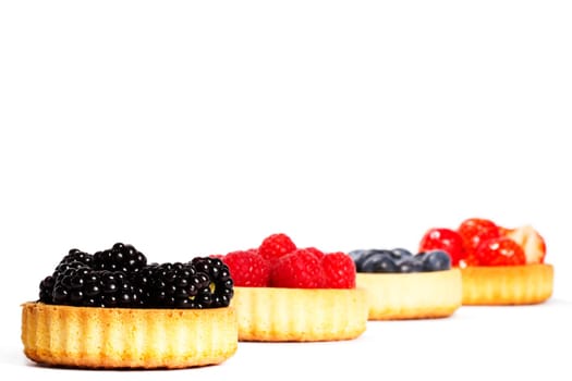 Blackberries in tartlets in front of other berries on white background