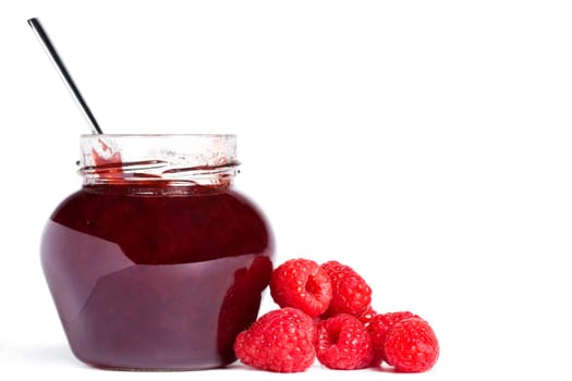 Jam jar with raspberries and a spoon on white background