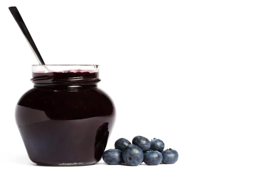 Jam jar with blueberries and spoon on white background
