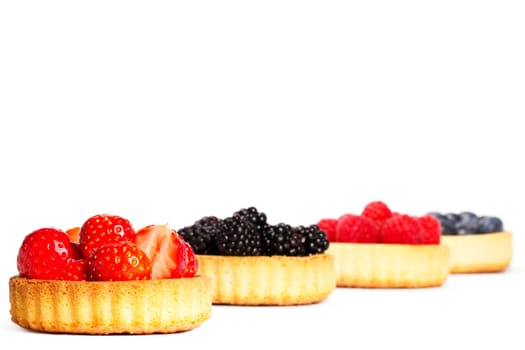 Strawberries on tartlet cake in front of other berries on white background