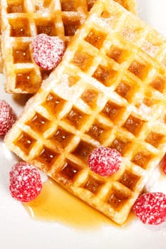 Sugared raspberries on waffles with syrup on white background
