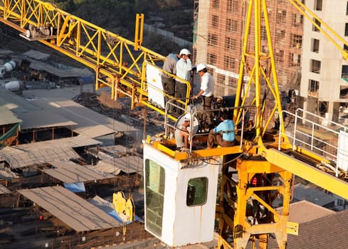 Mumbai, India, Men at work repairing faulty crane on high rise block, man using mobile phone, urban landscape