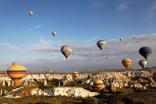 Cappadocia, Turkey: June 2011 - skies over Cappodiocia Kapadokya filled with colorful hot air ballons, blue sky, wispy clouds, mountain landscape and rough terrain