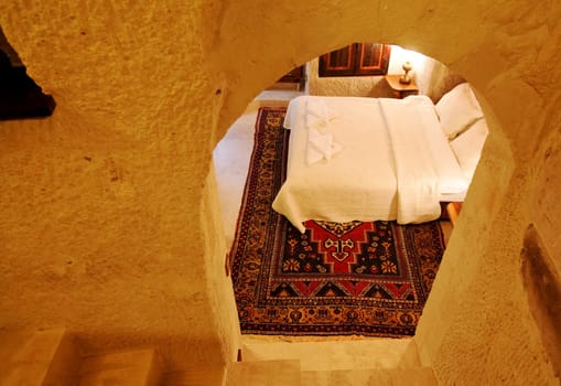 renovated limestone cave bedroom interior design and layout fully furnished with white bed linen and woven carpet, landscape, crop margins and cop space, veiwd through an archway