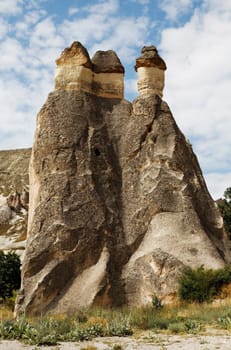 close-up three fairy chimneys group in the wilderness of Cappadocia, Turkey surrounded by minerals and wild bushes. Portrait, crop space and copy space with blue cloudy sky