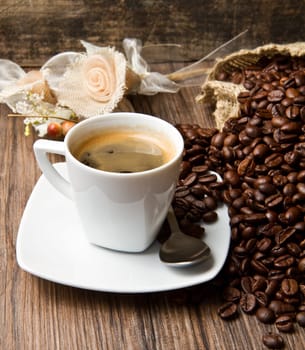 Coffee cup with burlap sack of roasted beans on rustic table