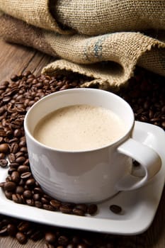 Coffee cup with burlap sack of roasted beans on rustic table