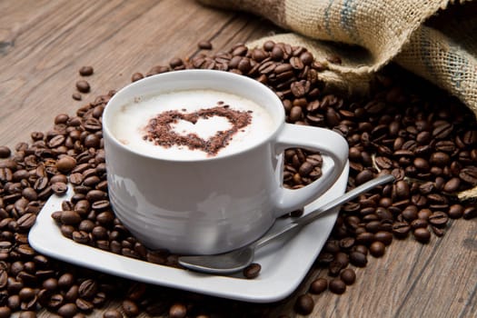 Coffee cup with burlap sack of roasted beans on rustic table