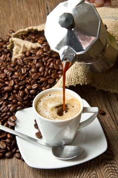Coffee cup with burlap sack of roasted beans on rustic table