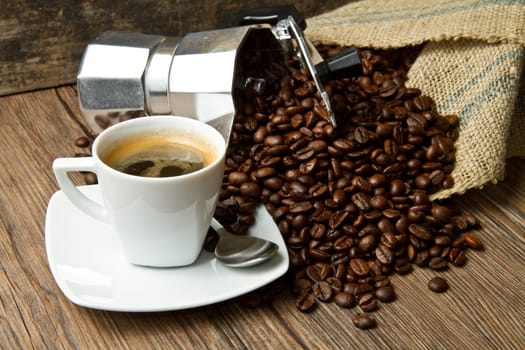 Coffee cup with burlap sack of roasted beans on rustic table