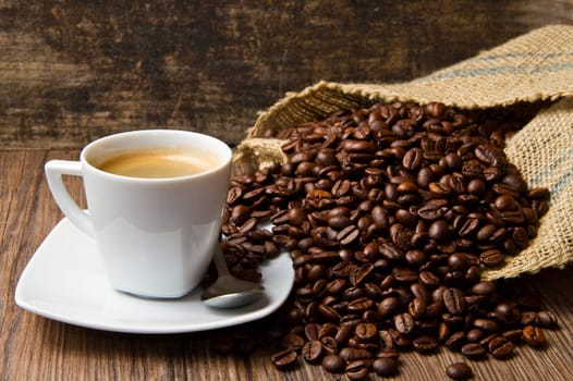 Coffee cup with burlap sack of roasted beans on rustic table