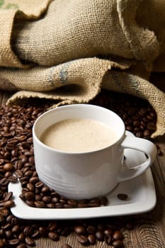 Coffee cup with burlap sack of roasted beans on rustic table