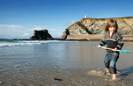 Beach holiday in Cornwall, England. St Agnes coastline with child in water with spade or shovel