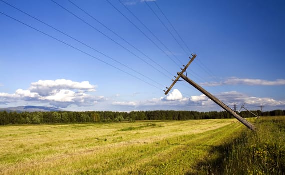 Landscape, falling telegraph poles on mown field on a background of forest and sky with clouds