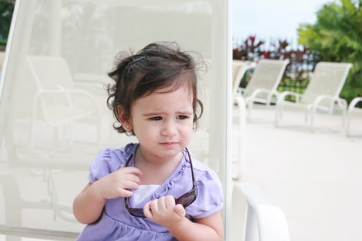 cute toddler girl in summer clothes and sunglasses lyiing on a lounge and relaxing in tropic ocean background