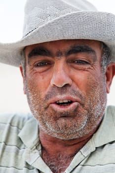 Goreme, Turkey - June, 2011: Portrait of weather beaten unshaven face of a senior gent Turkish builder with a dusty tanned face wearing a wide rimmed hat for protection against the sun, vertical close crop