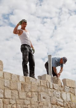 Goreme, Cappadocia, Turkey - June, 2011: Men at work, handsome body toned Turkish builder saluting under a bright cloudy sky from an elevated position. Brickie laying bricks.