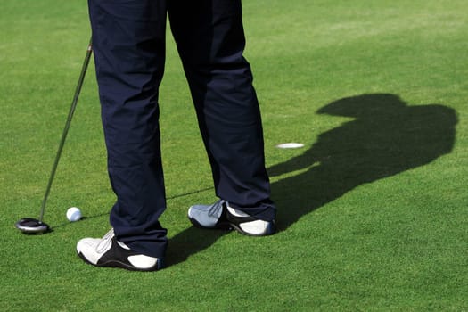 A man is standing on the green of a golf course. He is putting the ball into the hole.