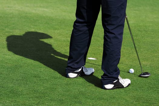 A man is standing on the green of a golf course. He is putting the ball into the hole.