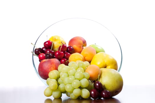 Glass bowl of fruit on a table against white background