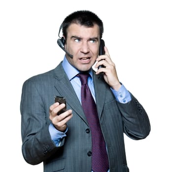 Portrait of businessman wearing headset and using mobile phone busy with multiple telephone in studio isolated white background