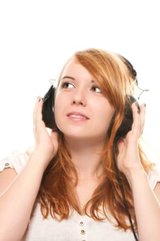 A dreamy young redhead woman with headphones is listening to music against a white background