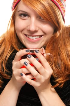 Young redhead woman in winter clothes warming herself at a glass of tea against a white background