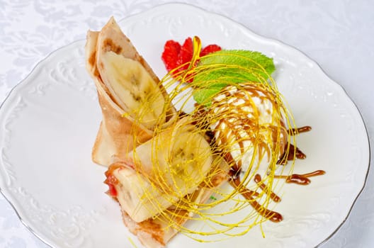Dessert of pancake with banana, ice-cream, caramel, strawberry and mint