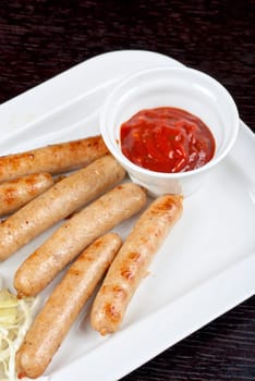 Grilled sausages with cabbage, greens and tomato sauce on white plate