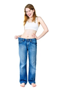 Happy fit young woman in loose old jeans after losing weight isolated on white