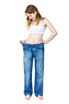 Smiling fit young woman in loose old jeans after losing weight isolated on white