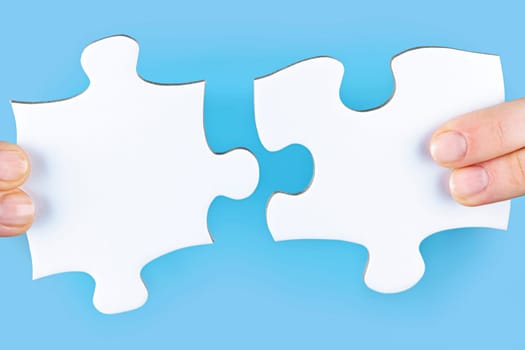 Fingers joining large white blank jigsaw puzzle pieces