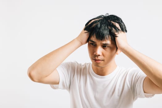 An Asian man, visibly stressed and unwell, holds his head with a pained expression, depicting the agony of a headache. Studio shot isolated on white background, conveying his suffering.