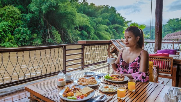 Asian woman having breakfast table at a tropical beach house on the River Kwai in Thailand.Wooden floating raft house in river Kwai Kanchanaburi, Thailand