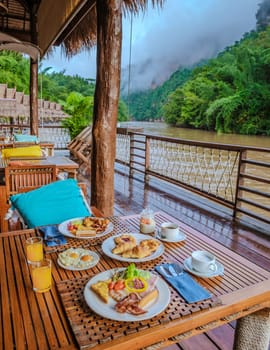breakfast table at a tropical beach house on the River Kwai in Thailand.Wooden floating raft house in river Kwai Kanchanaburi, Thailand, breakfast with eggs bread and coffee