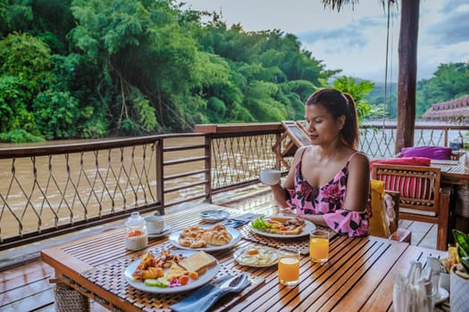 Asian woman having breakfast table at a tropical beach house on the River Kwai in Thailand.Wooden floating raft house in river Kwai Kanchanaburi, Thailand