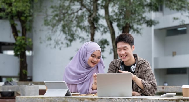 Happy multiethnic group of teenage students talking about the homework after the class at university campus. Two young people smiling, having a friendly conversation together.