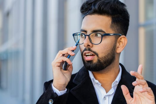 Stylish Indian businessman having remote conversation communicate speaking by smartphone outdoor. Arabian Hindu freelancer guy talking on phone standing downtown city street. Business people lifestyle