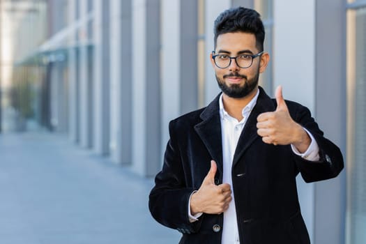 Like. Happy Indian businessman raises thumbs up agrees gives positive reply recommends advertisement likes good idea feedback, celebrating success victory. Arabian Hindu freelancer guy in city street
